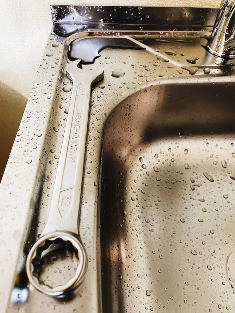 Pipe wrench resting on a wet stainless-steel sink