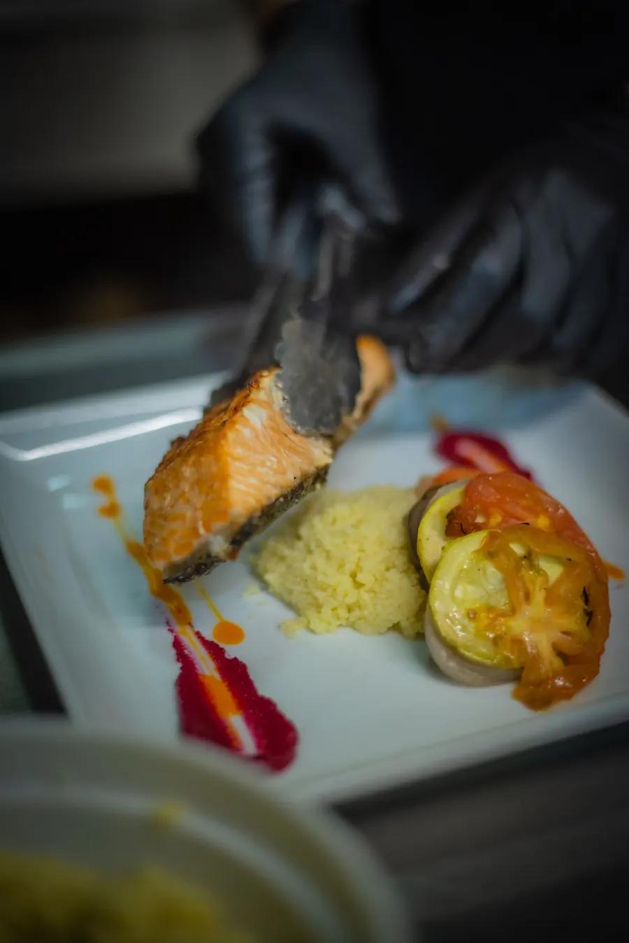 Chef plating charred salmon with grains and greens